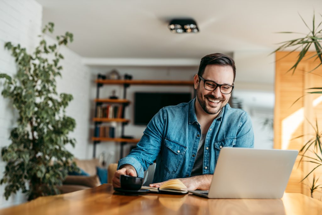 Entrepreneur at home office, looking at laptop and drinking cup of coffee